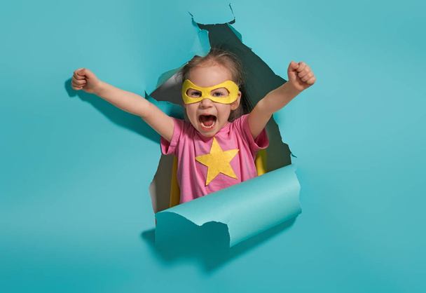 Little child playing superhero. Kid on the background of bright blue wall. Girl power concept. Yellow, pink and  turquoise colors. - Foto, Imagem
