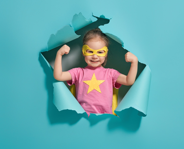Little child playing superhero. Kid on the background of bright blue wall. Girl power concept. Yellow, pink and  turquoise colors. - Photo, image
