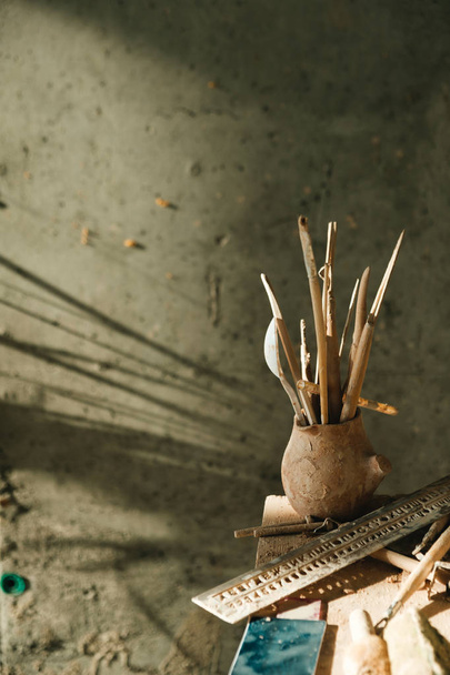 Tarro sucio de cerámica hecha a mano de un alfarero lleno de instrumentos, cepillos, reglas
 - Foto, imagen