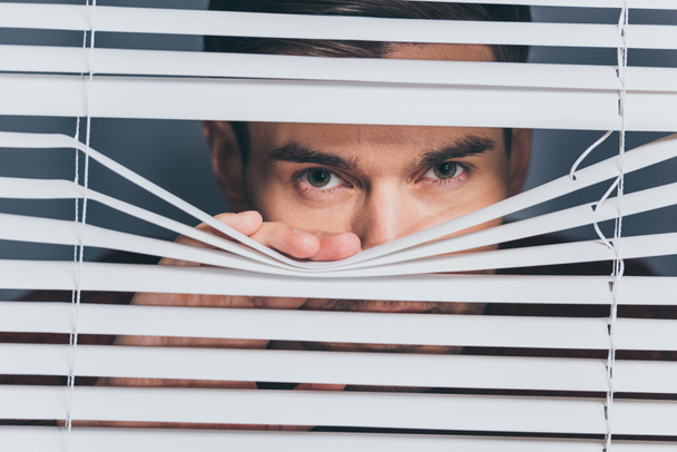 suspicious young man looking at camera through blinds, mistrust concept - Photo, Image
