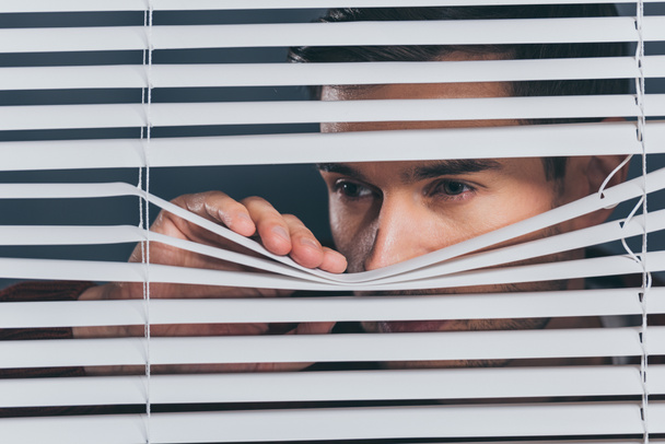 suspicious young man looking away and peeking through blinds - Photo, Image