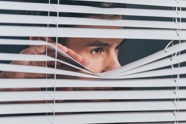 Close-up beeld van jonge man spionage en kijken weg door blinds - Foto, afbeelding