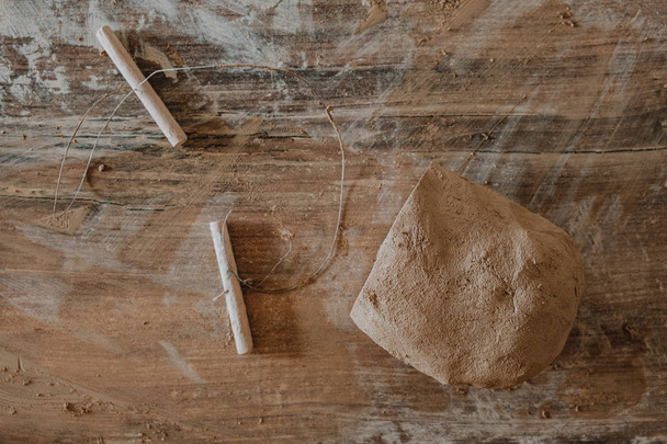 Pedaço de barro cortado com fio deitado na mesa de madeira preparada para a roda de cerâmica
 - Foto, Imagem