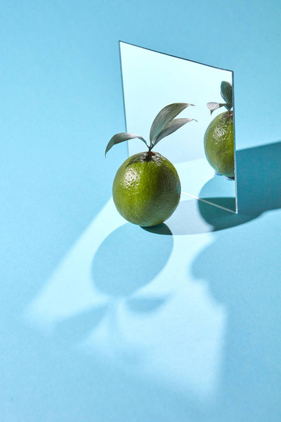 Composition from a mirror, and lime with leaves on a blue background with reflection of shadows and copy space. Organic fruit - Foto, Imagen