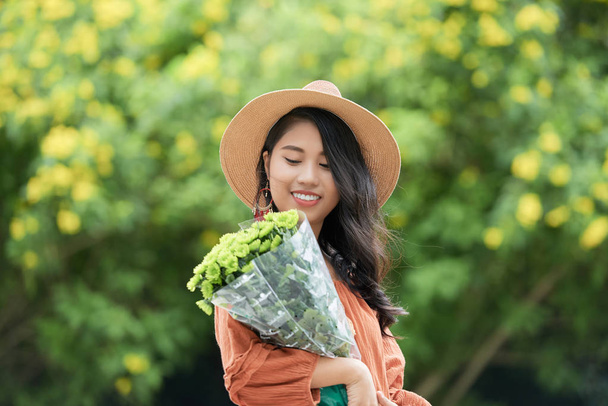 Красивая привлекательная молодая вьетнамская женщина, смотрящая на красивые цветы в руках
 - Фото, изображение
