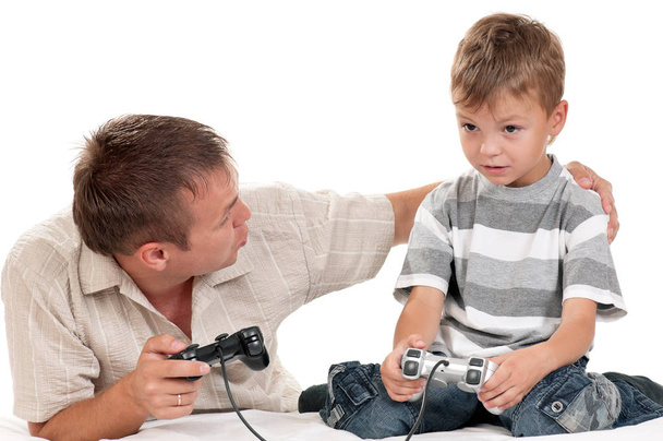 Μπαμπάς και γιος κρατώντας τα χειριστήρια και παίζοντας βιντεοπαιχνίδια στην κονσόλα μαζί. Οικογένεια - ο πατέρας και αναστατωμένος αγόρι τυχερών παιχνιδιών σε λευκό φόντο. Ο άνθρωπος με το παιδί παίζοντας παιχνίδι στον υπολογιστή. - Φωτογραφία, εικόνα