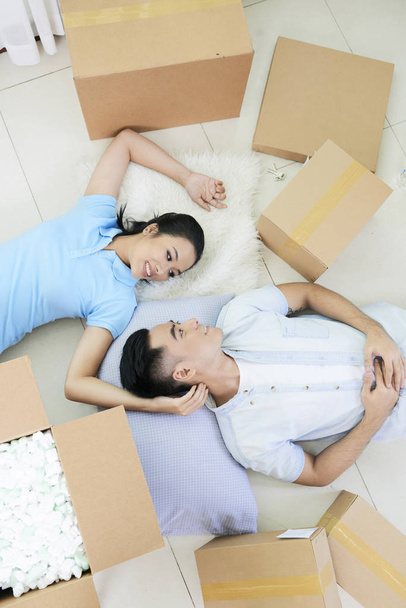 De arriba tiro de asiático hombre y mujer en el amor acostado en el suelo entre cajas mientras se mueve
 - Foto, imagen