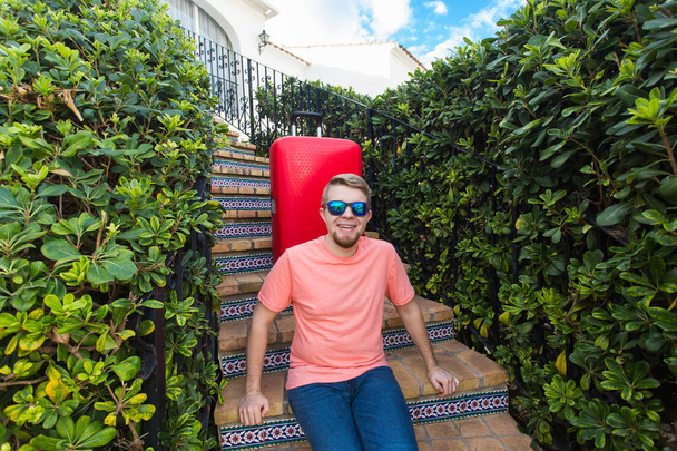 Vakantie, reizen en toerisme concept - knappe man met rode koffer zittend op een trap - Foto, afbeelding