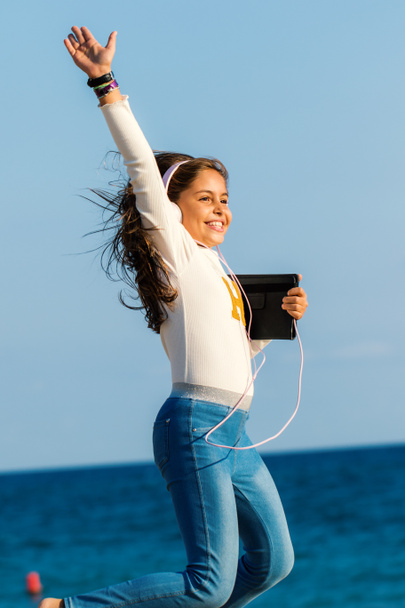 Close up action ritratto di sorridente tween ragazza che salta con cuffie e tablet sulla spiaggia
 - Foto, immagini