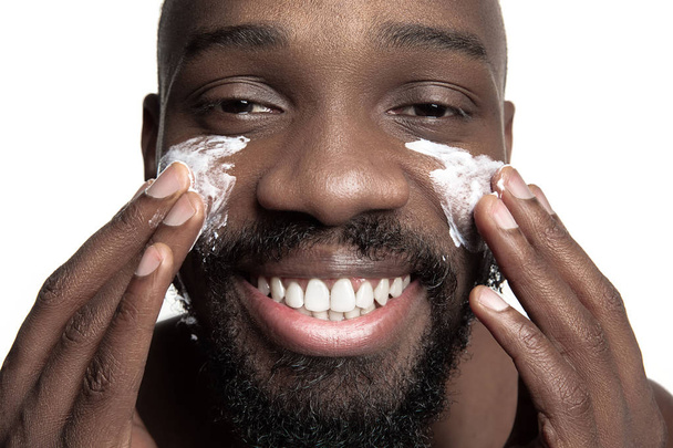 Young african-american guy applying face cream under his eyes on white background - Fotografie, Obrázek