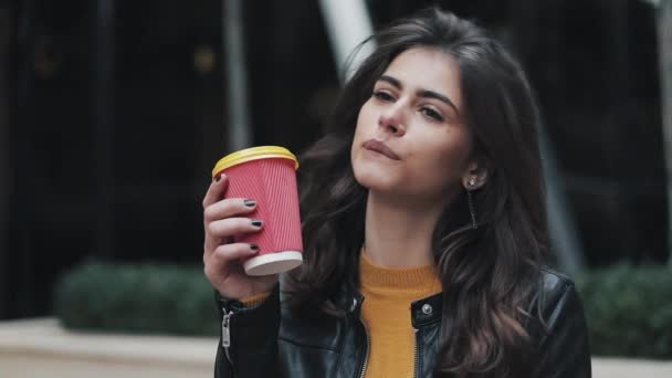 Beautiful young woman with an attractive appearance, adorable look and autumn jacket in the city. Amazing view of business lady with a cup of coffee walking down the city street - Video