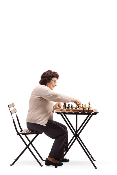Full length profile shot of a senior woman moving a chess figure isolated on white background - Valokuva, kuva