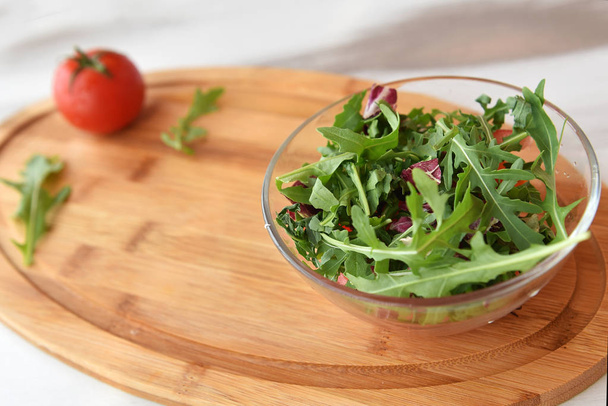 on a wooden background, a plate with fresh herbs, arugula and cabbage. near a tomato. space for text - Photo, Image