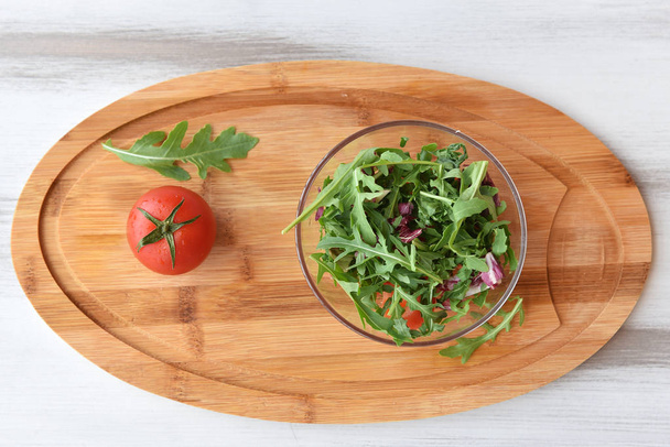 on a wooden background, a plate with fresh herbs, arugula and cabbage. near a tomato. space for text - Fotoğraf, Görsel