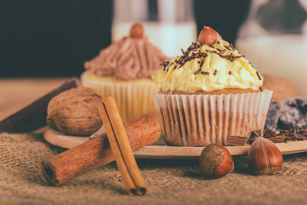 Nahaufnahme eines Schoko-Muffin-Cupcake mit Vanillecreme und Haselnüssen auf einem Holzbrett - Bild - Foto, Bild