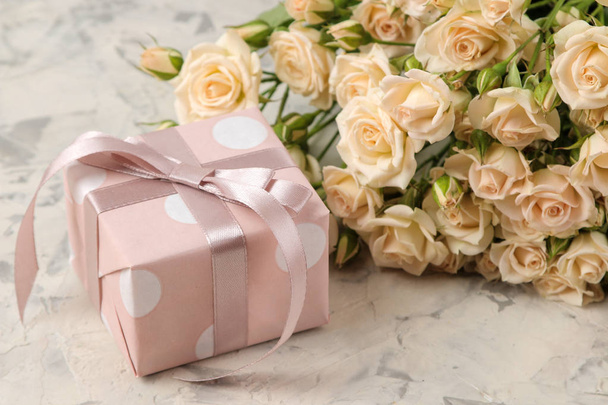 A bouquet of beautiful tender mini roses and a gift box on a light concrete background. holidays. presents - Zdjęcie, obraz
