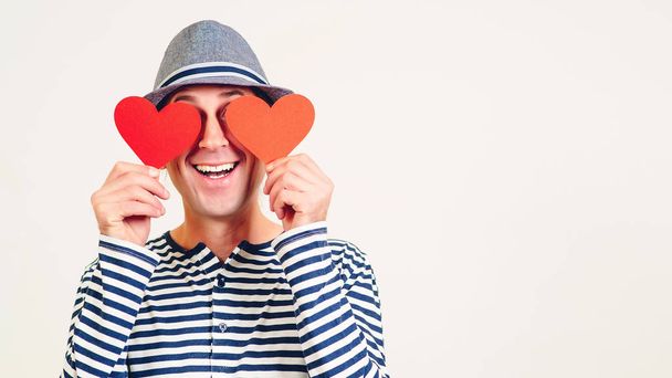 Happy Valentines Day. Funny man covers eyes with red hearts. Happy man in love. Romantic guy holds valentine cards. Be my valentine. Boyfriend showing love fun affection. Copy space. - Фото, изображение