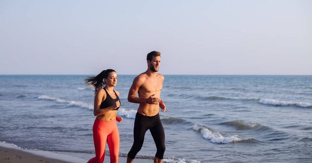 Handsome Caucasian man and beautiful woman running on sandy beach. - Foto, imagen