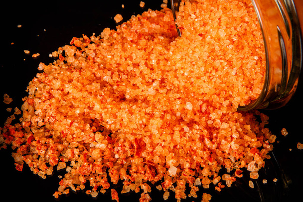 makroiso oranssi luonnonmukainen merisuola kaadetaan pienestä lasipurkista mustalla peilitaustalla
 - Valokuva, kuva