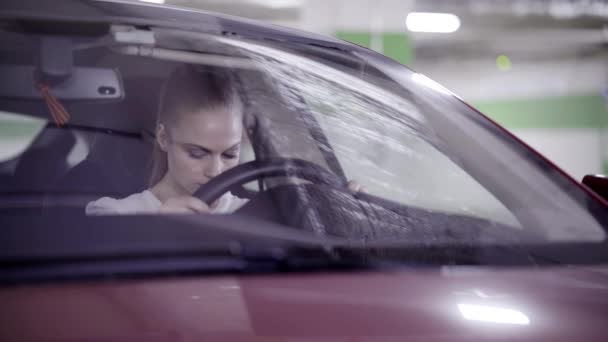 Chica bonita en camisa blanca se sienta en coche rojo y sostiene el volante en el garaje
 - Imágenes, Vídeo