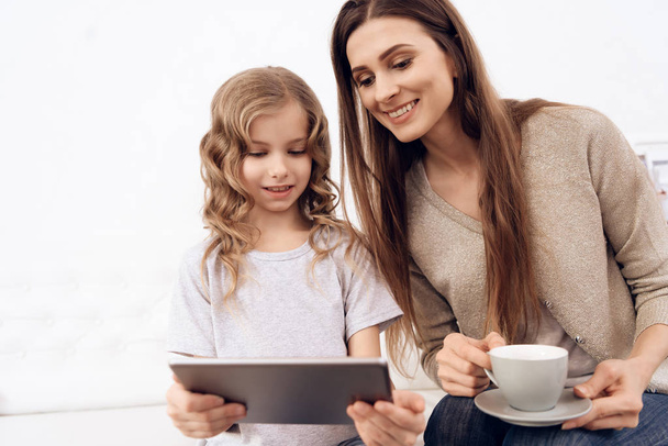 Little curly girl with beautiful brown hair mother choose hairstyle on tablet. - Foto, imagen