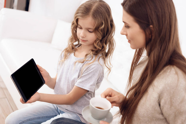 Little curly girl with beautiful brown hair mother choose hairstyle on tablet. - Foto, immagini