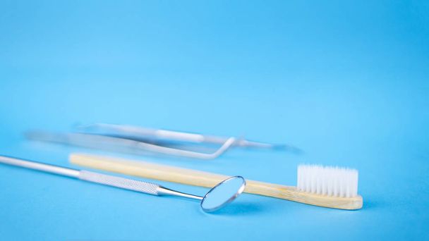 Zahnarztspiegel und -haken, weiße Holzzahnbürste. Dentalhygiene und Gesundheitskonzept. blauer Hintergrund mit Kopierraum für Text - Foto, Bild