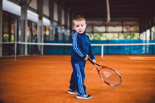 Szeptember 20, 2016-ban. Ukrajna, Kiev.theme a gyermekek testi fejlődését. Kaukázusi gyermek fiú 3 - 4 év régi jelent a tenisz ütő labda kéz tennis narancssárga kéreg háttér tnet kék sport ruha. - Fotó, kép