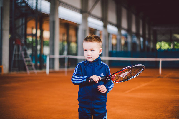 Szeptember 20, 2016-ban. Ukrajna, Kiev.theme a gyermekek testi fejlődését. Kaukázusi gyermek fiú 3 - 4 év régi jelent a tenisz ütő labda kéz tennis narancssárga kéreg háttér tnet kék sport ruha. - Fotó, kép