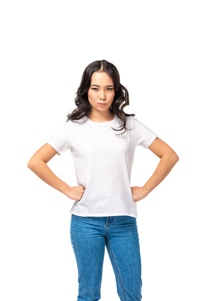 Beyaz t-shirt ve kot üzerinde beyaz izole kalça üzerinde el ele tutuşarak kızgın Asyalı kadın  - Fotoğraf, Görsel
