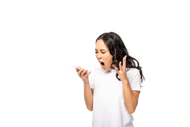 Yelling asian girl in white t-shirt and blue jeans using smartphone isolated on white - Фото, изображение