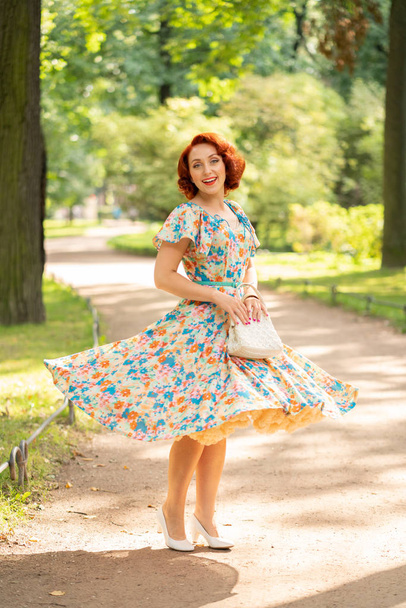 cute caucasian girl with red bob haircut in retro dress enjoying life in city Park in summer sunny day - Фото, изображение