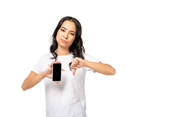 tyytymätön aasialainen nainen tilalla älypuhelin tyhjä näyttö ja osoittaa peukalo alas eristetty valkoinen
 - Valokuva, kuva