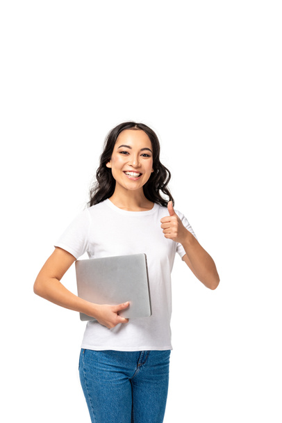 Smiling pretty video chat woman in white t-shirt and blue jeans holding laptop and showing thumb up isolated on white - Photo, image
