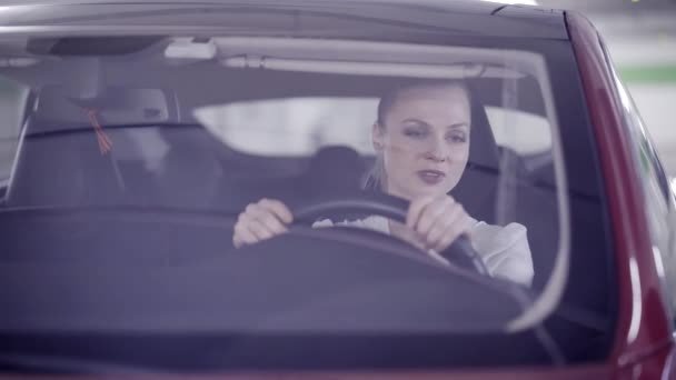 Cute female with ponytail sitting in red car behind wheel when it starts smoking - Séquence, vidéo