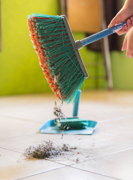 Uma mulher varre poeira e sujeira do chão enquanto limpa a casa
 - Foto, Imagem