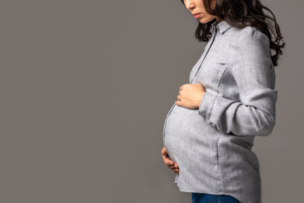 Partial view of serious pregnant asian woman holding tummy with hands isolated on grey - Φωτογραφία, εικόνα
