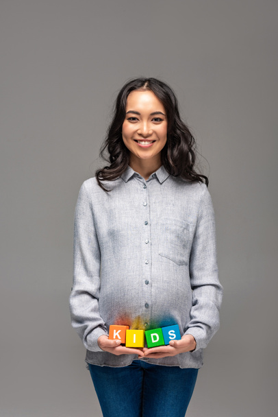 Усміхнена вагітна молода азіатка тримає кубики алфавіту зі словом діти ізольовані на сірому
 - Фото, зображення