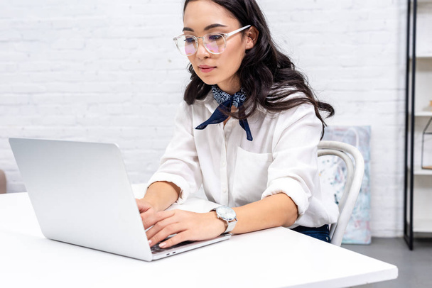Attentive asian freelancer in glasses using laptop at home workplace - Photo, Image