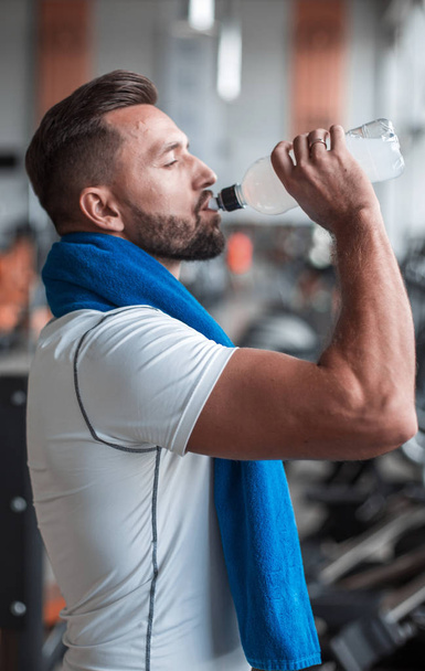 Young adult man drinking bottle of water on trreadmill in gym. - Fotografie, Obrázek