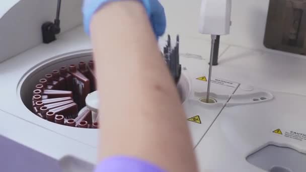 εργαστήριο εργαζόμενος κάνει μια εξέταση αίματος. φορτία των σωλήνων στο μηχάνημα. Ο βοηθός φόρτωσης το φιαλίδιο σε εργαστήριο φυγοκέντρησης. Αλλαγή φιαλίδια αίματος. - Πλάνα, βίντεο