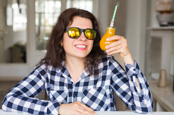 Táplálkozás, az egészséges életmód és a méregtelenítés koncepció - fiatal nő, napszemüveg, narancslé az üveg néz ki, mint egy lámpa. - Fotó, kép