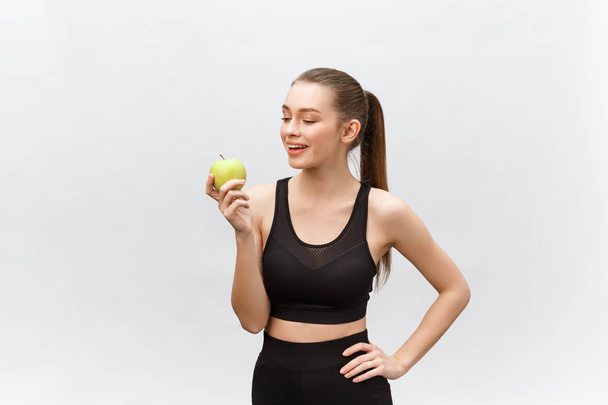 Portrait of a happy young caucasian woman holding and eating green apple over white background - Foto, Imagem