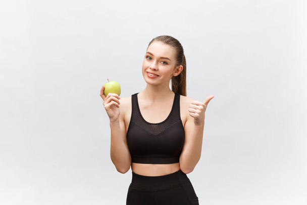 Portrait of a happy young caucasian woman holding and eating green apple over white background - Foto, Imagen