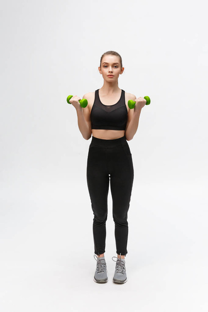 Portrait of Caucasian woman on white background wearing black fitness separate and excercising with dumbells. - Zdjęcie, obraz