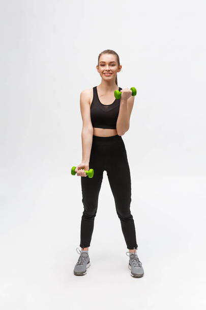 Portrait of Caucasian woman on white background wearing black fitness separate and excercising with dumbells. - Photo, Image
