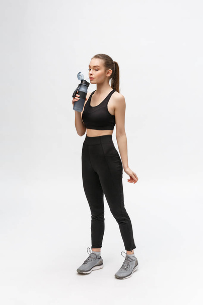 Side view full length portrait of a young healthy sports woman holding a water bottle isolated on a white background - Foto, immagini