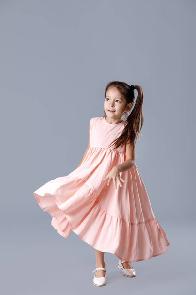 little girl in pink dress posing on gray background. - Photo, image