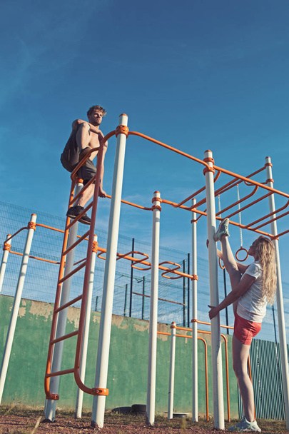 Sport workout and pilates concept. Sport couple training in metal jungle gym. Man athlete climb on top and woman split leg. Sportsman and sportswoman at monkey bars - Zdjęcie, obraz
