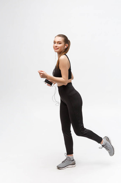 Sport woman. Young beautiful woman in sport clothes. Portrait full length sitting in headphones listening music. - Photo, Image